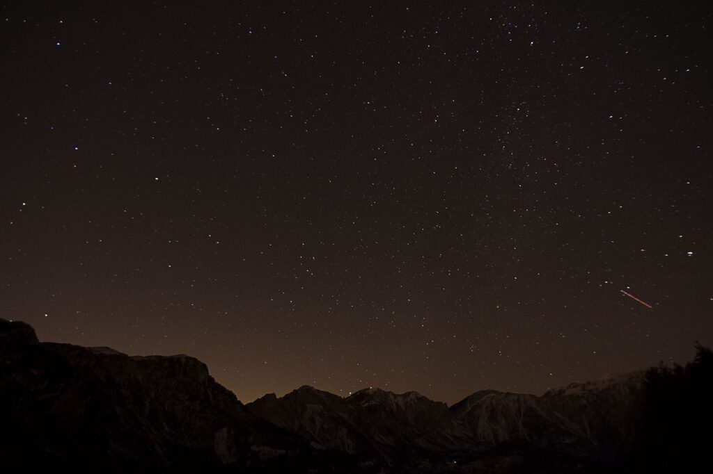 Ciel étoilé au-dessus de montagnes sombres avec une trace lumineuse.
