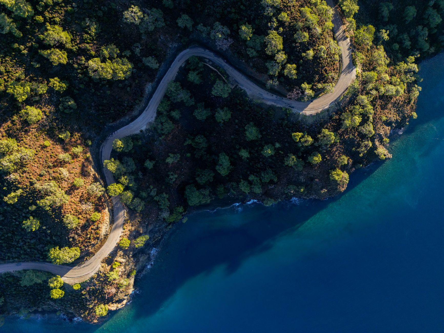 Vue aérienne d'une route sinueuse longeant une côte boisée et un plan d'eau.
