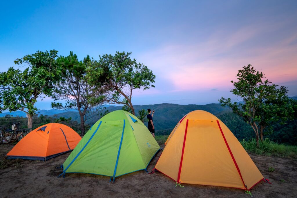 Trois tentes de camping colorées sous un ciel crépusculaire avec des montagnes en arrière-plan.