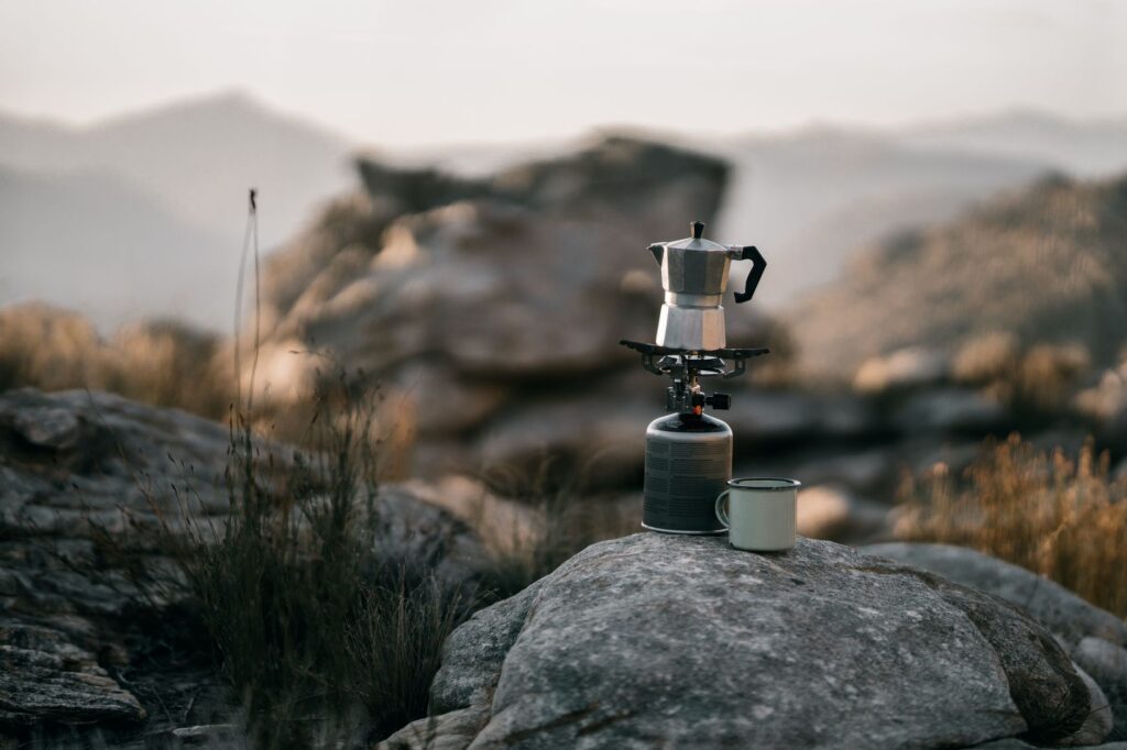 Cafetière italienne et réchaud de camping sur un rocher, montagnes floues