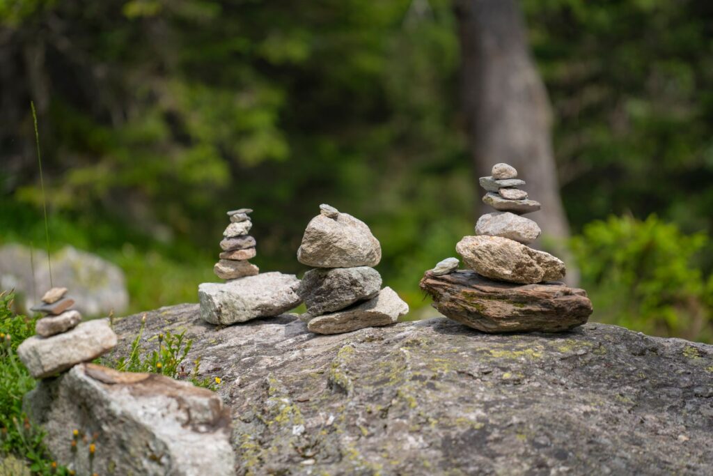 Trois cairns en pierre sur un rocher, avec un fond végétal flou.