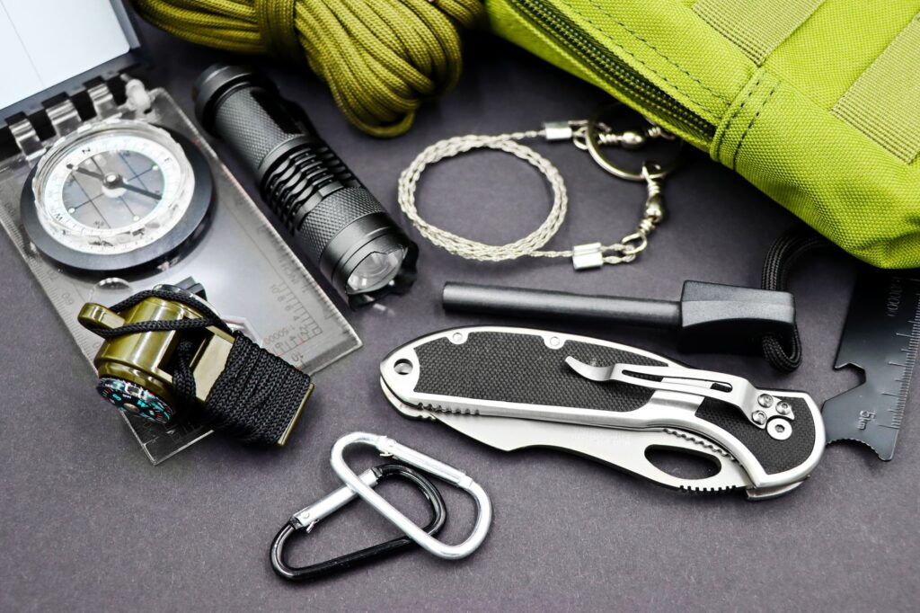 Équipement de survie et randonnée : boussole, lampe, sifflet, couteau, mousquetons, sac.
