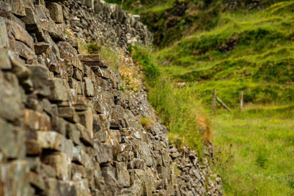 Un mur de pierres sèches devant une colline herbeuse verte avec un poteau de clôture.