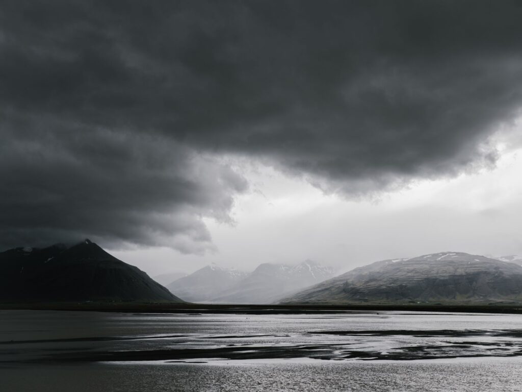 Sombre paysage de montagnes sous un ciel orageux avec un plan d'eau.