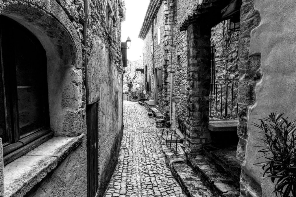 Ruelle étroite pavée en noir et blanc, murs en pierre, maisons traditionnelles.