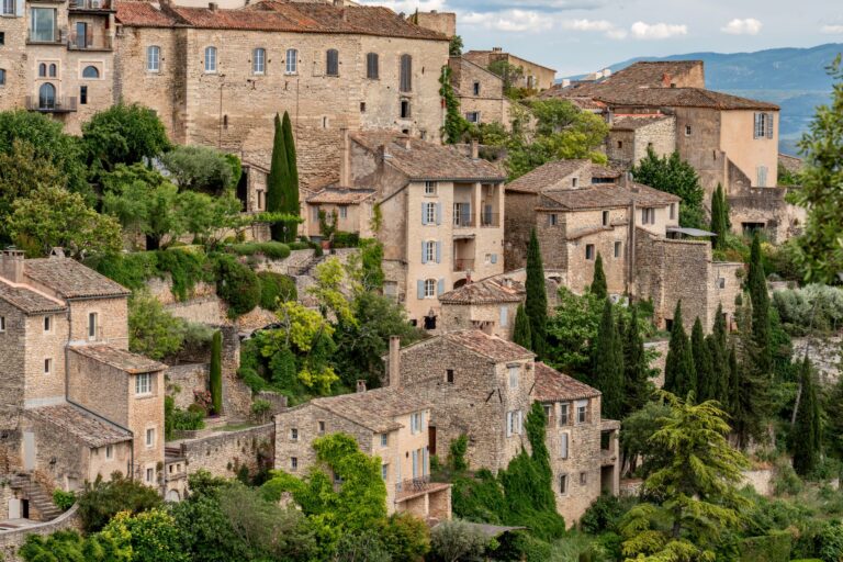 Village perché de maisons en pierre et tuiles rouges, entouré de verdure luxuriante.