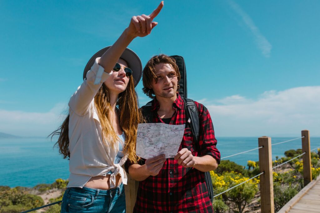 Deux randonneurs regardent une carte et la femme pointe le ciel au-dessus de la mer.