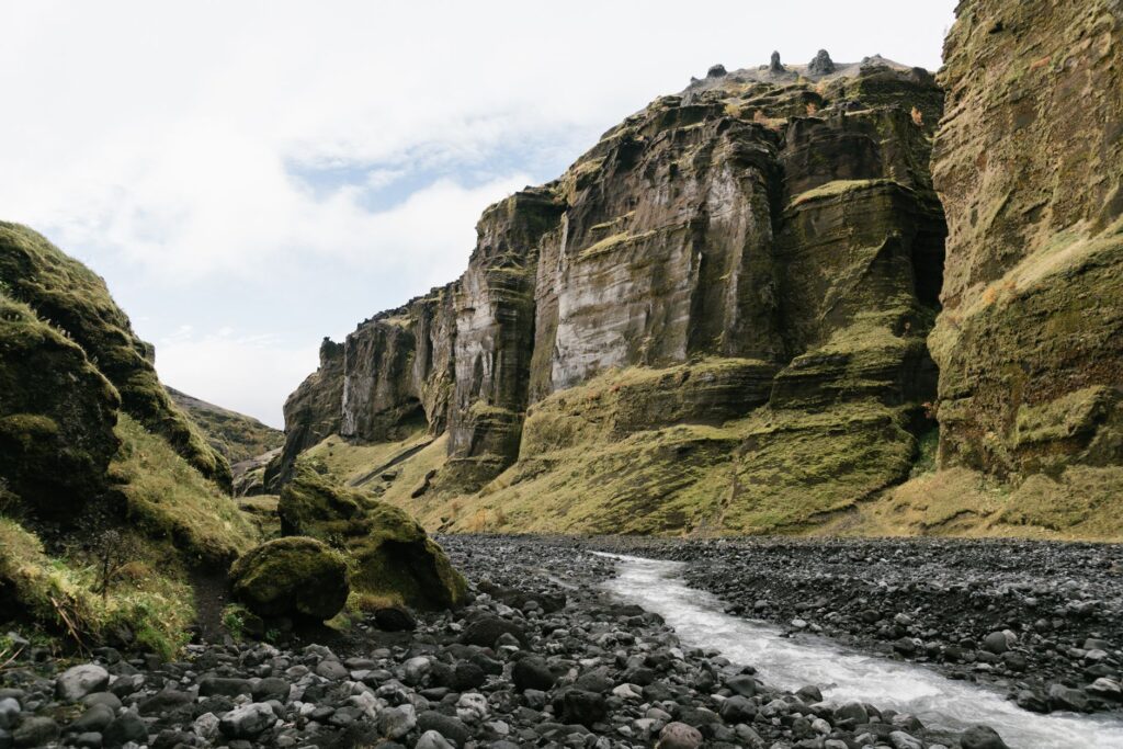 Rivière à travers un canyon rocheux et moussu sous un ciel nuageux.